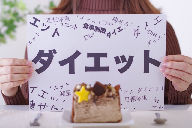 ケーキを前にダイエットと書かれたボードを掲げる女性